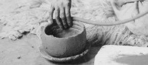 Person is making a bowl by the coiling technique of pottery. About half of the pot has been made and smoothed out, and you can see some of the last rings of coils as they snake the next coil around the pot. 