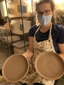 Myself holding two plates. On the left, the top of the plate is shown to be trimmed, with clean edges and a spiral pattern on the face of the plate. The left plate looks much more rough, no spiral pattern