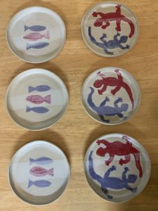 6 white plates, 3 with two blue fish and one red fish in the middle of the plates, 3 plates with one red salamander and one blue salamander chasing eachother's tails
