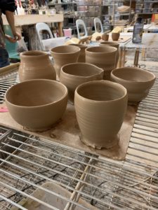 side view of several light brown pots and bowls of various sizes on light brown cork board