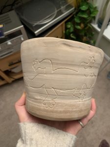 light brown pot held in hand with salamander carved into side of pot.